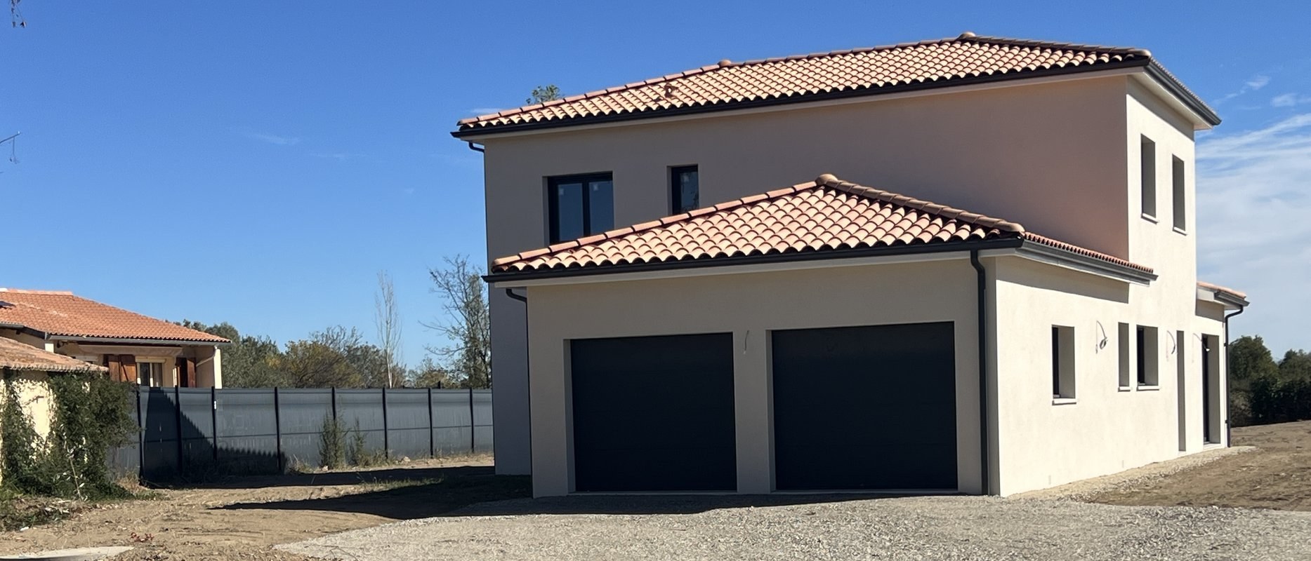 Villa R+1 livrée à Seysses, enduit clair, toitures quatre pentes en tuiles canal et garage double à portes sectionnelles anthracite sur cour gravillonnée