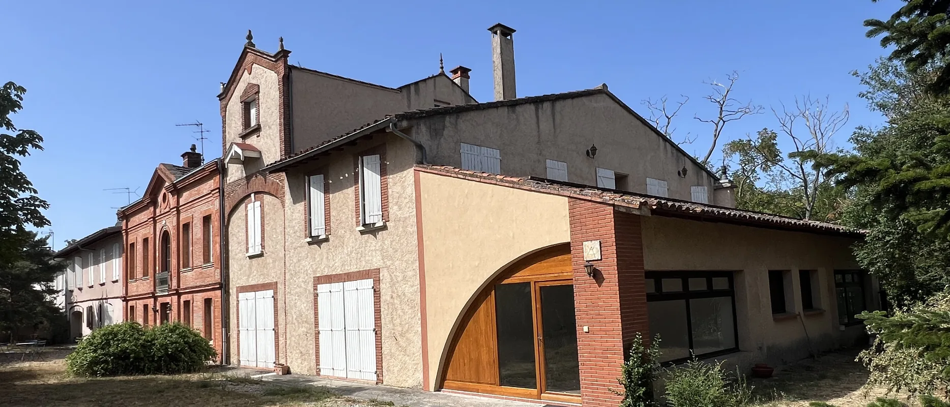 Vue d'ensemble de la bâtisse ancienne de Venerque depuis le jardin, corps en R+2 à pignon de brique et aile en R+1 avec baie cintrée en chêne